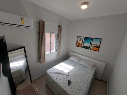 Cozy guest bedroom with double bed, floral bedding, split air conditioner, full-length mirror, and framed coastal artwork on the walls.