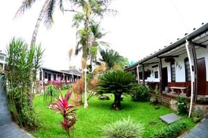 Lush tropical garden courtyard surrounded by white bungalows, featuring green lawns, palm trees, and colorful foliage.