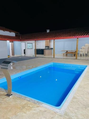 Illuminated blue pool at night with deck, water feature, and patio dining area.