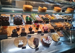 A mouth-watering glass display case filled with an assortment of artisan pastries, cheesecakes, cupcakes, and chocolate desserts.