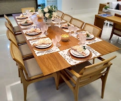 A beautifully styled dining room featuring a long wooden table set with elegant white plates, fine glassware, and a centerpiece of fresh white flowers, surrounded by classic wooden chairs.