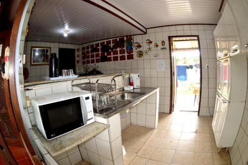 Compact kitchenette featuring a stainless steel sink, microwave, tiled countertops, white cabinets, and open door to a sunny exterior.