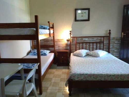 Spacious family bedroom featuring wooden bunk beds, a double bed with floral linens, bedside table, and tiled flooring.