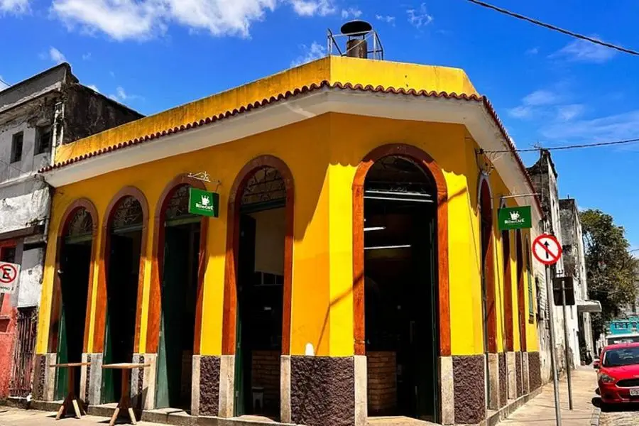 Striking yellow colonial-style building with arched doorways, stone base, green signage, and a bright blue sky.