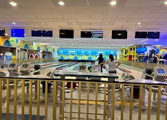 A fun and colorful bowling alley featuring multiple lanes, glowing screens, bright blue walls with painted murals, and arcade elements.