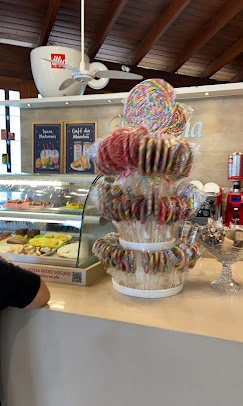 A charming cafe counter featuring a towering stand of fresh donuts, glass display cases of pastries, and a classic ceiling fan above.