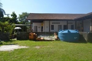 Wide exterior view of the Pousada Recanto Maresias showing the building facade, green lawn, and blue water tank.
