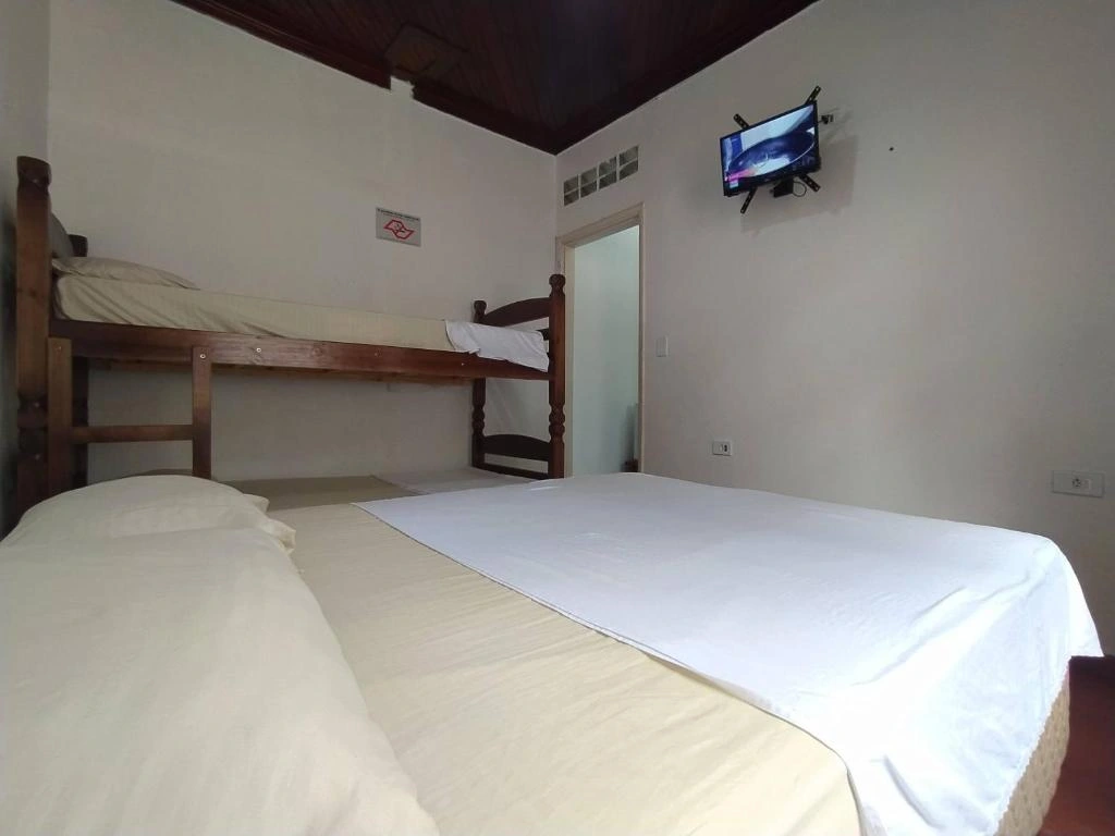 Interior of a family suite at Pousada Recanto Maresias with wooden bunk beds, a double bed, and wall-mounted TV.
