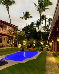 Illuminated pool and tropical garden at dusk with palm trees and bungalows.