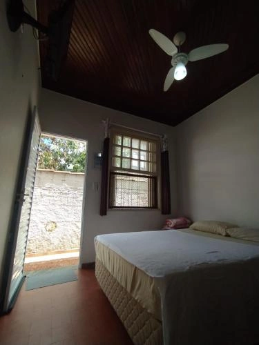 Simple guest bedroom featuring a double bed, dark wood ceiling with fan, and an open door leading to a garden area.