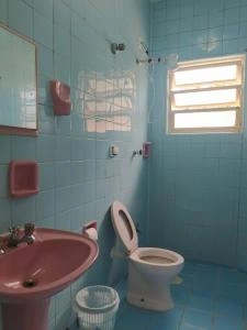 Clean bathroom interior with blue ceramic tiles, a pink pedestal sink, and a white toilet with open lid.